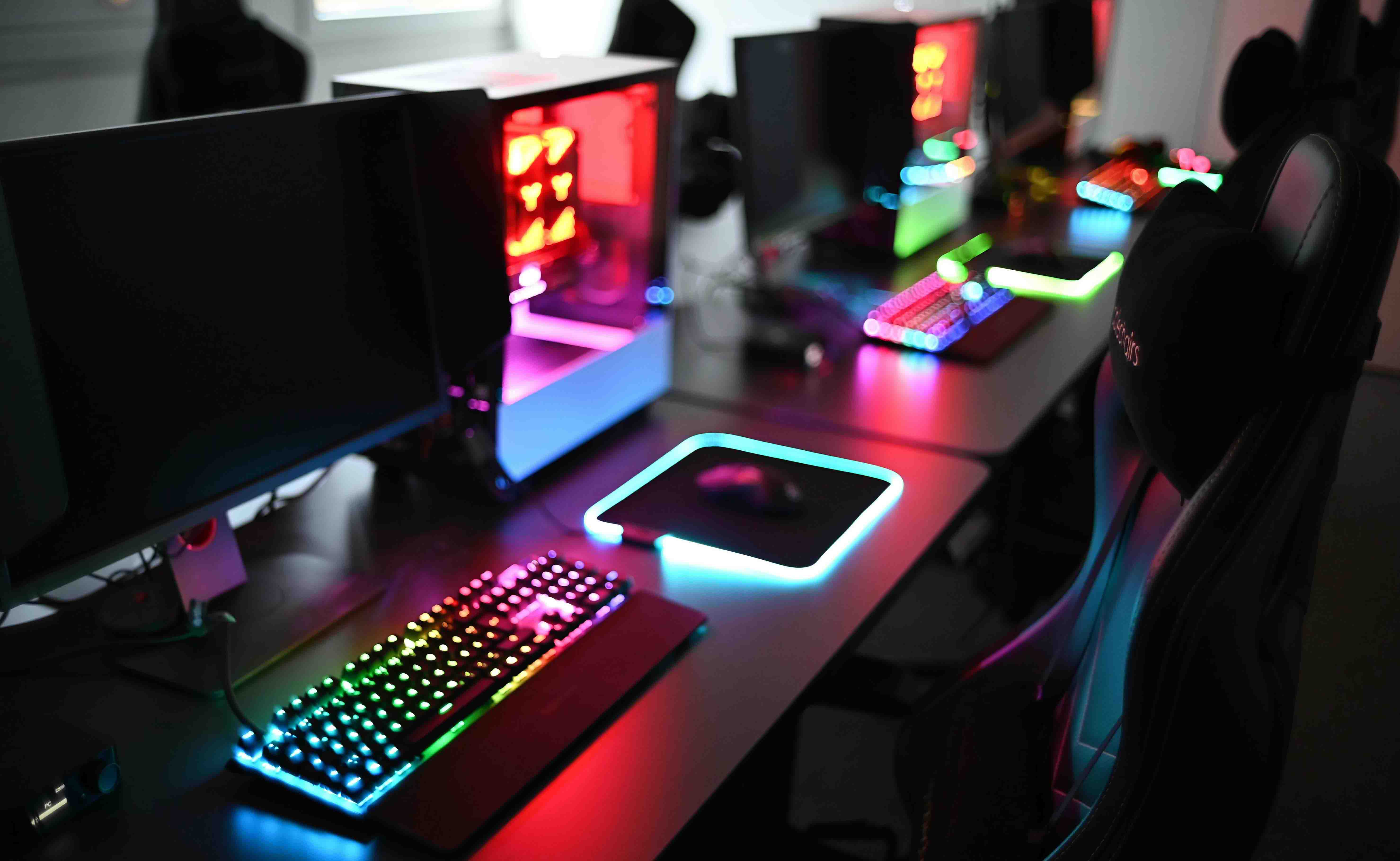 Computers with keyboards that have neon lights standing in a row on desks